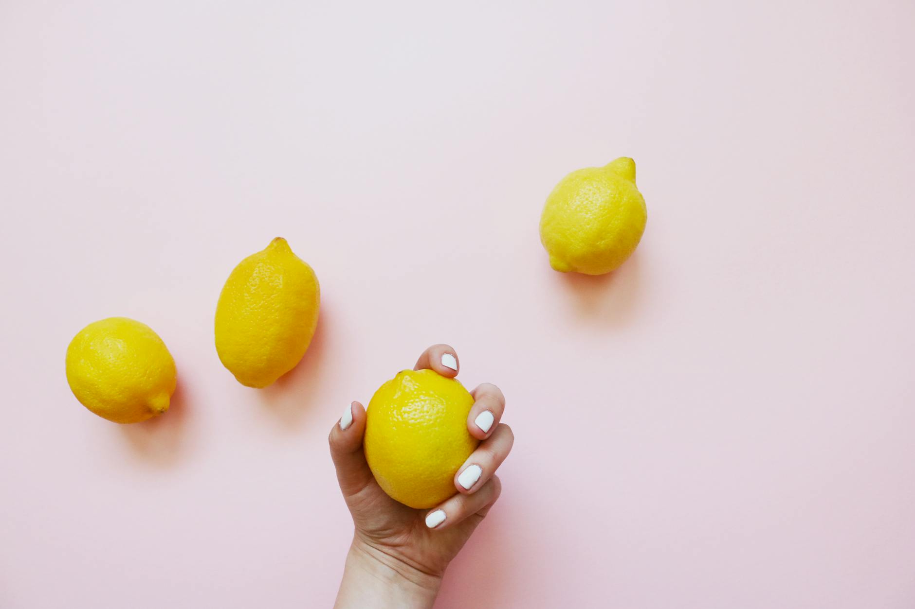 A hand holding a lemon on a soft pink background, symbolizing fresh pleasure after 50