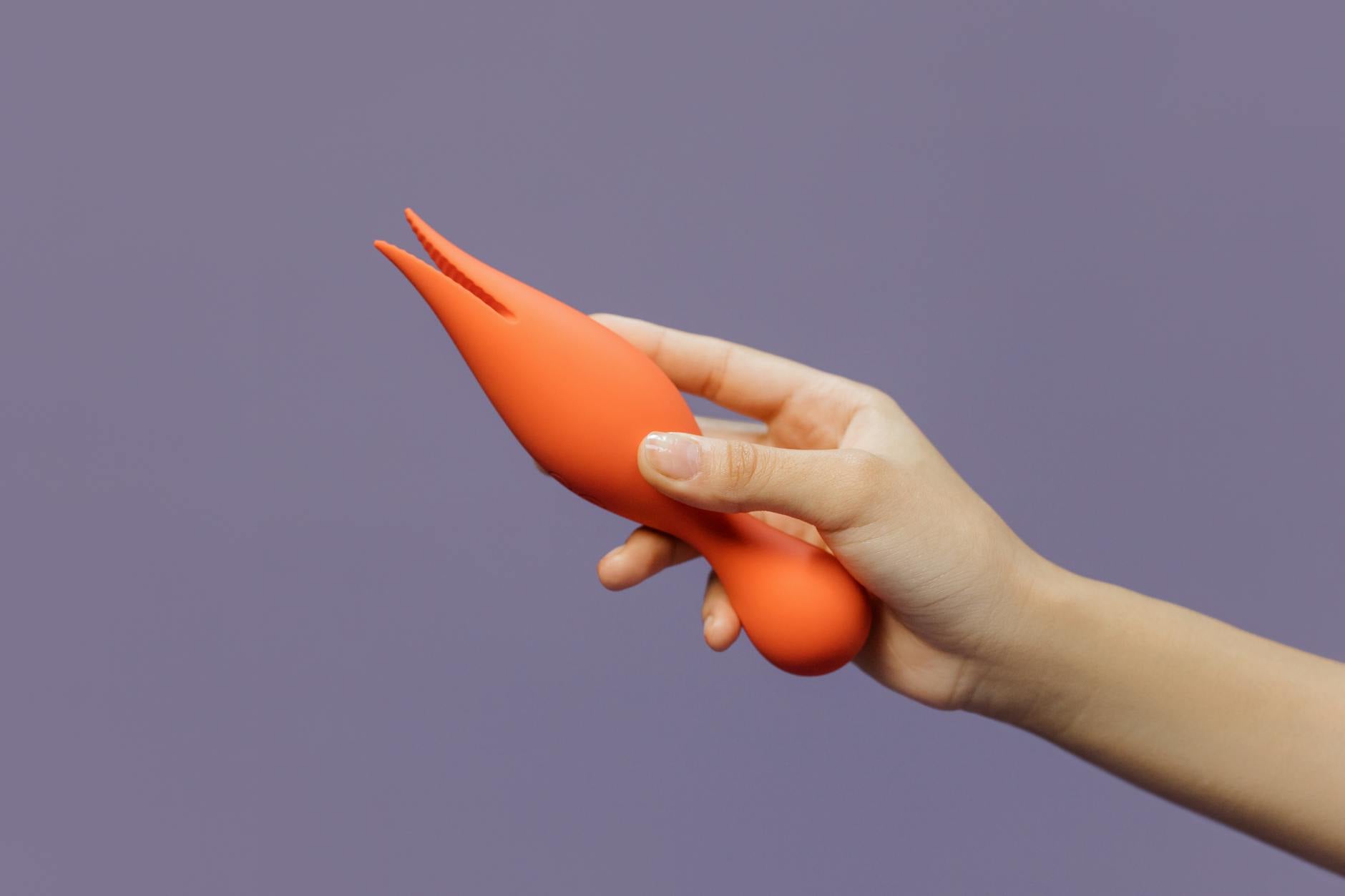 A close-up of a hand holding a vibrator against a minimalistic purple backdrop, showcasing sensuality and self-care