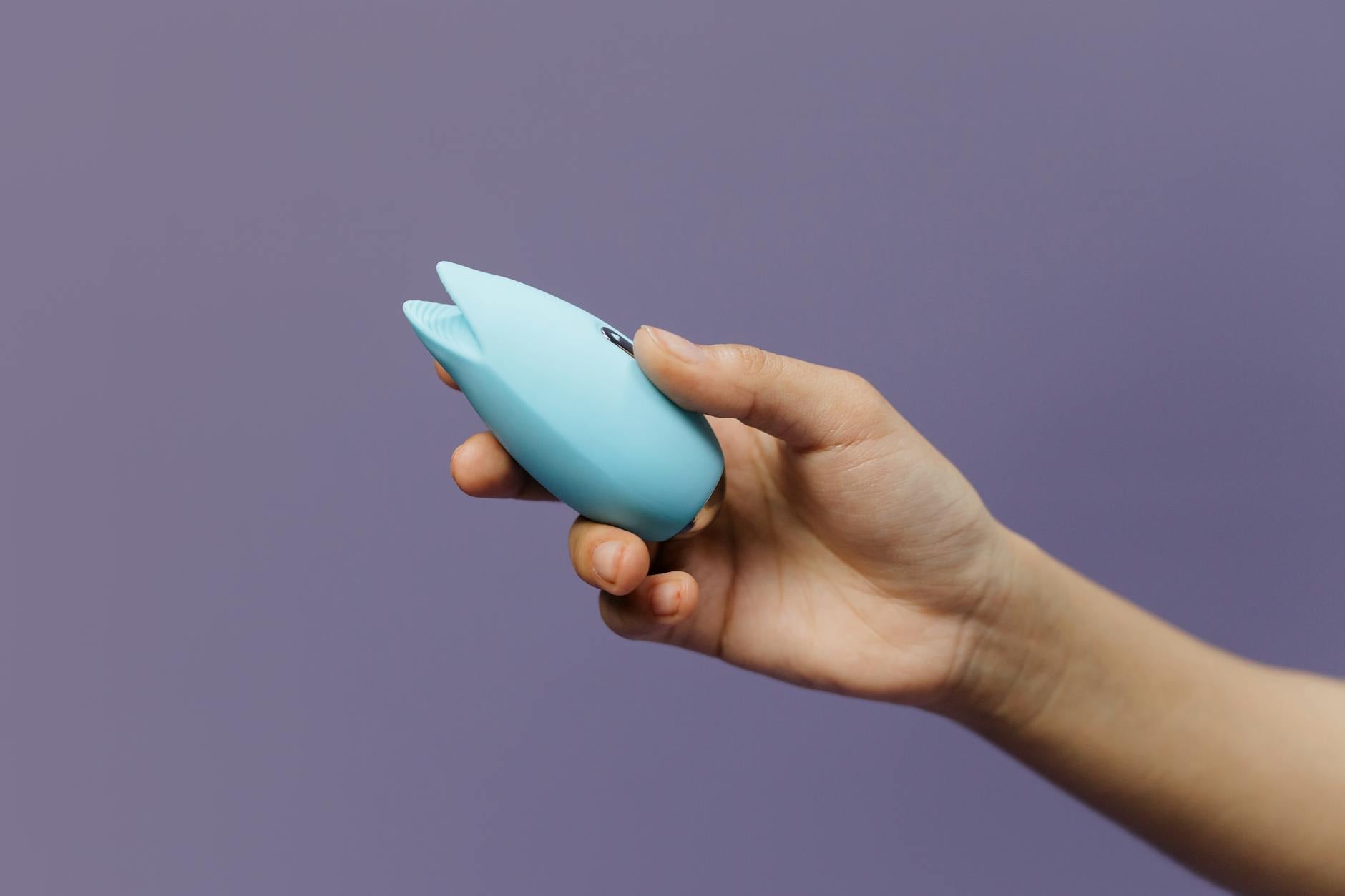 A blue lemon clitoral vibrator held in hand against a purple background, demonstrating tool for rebuilding sensitivity