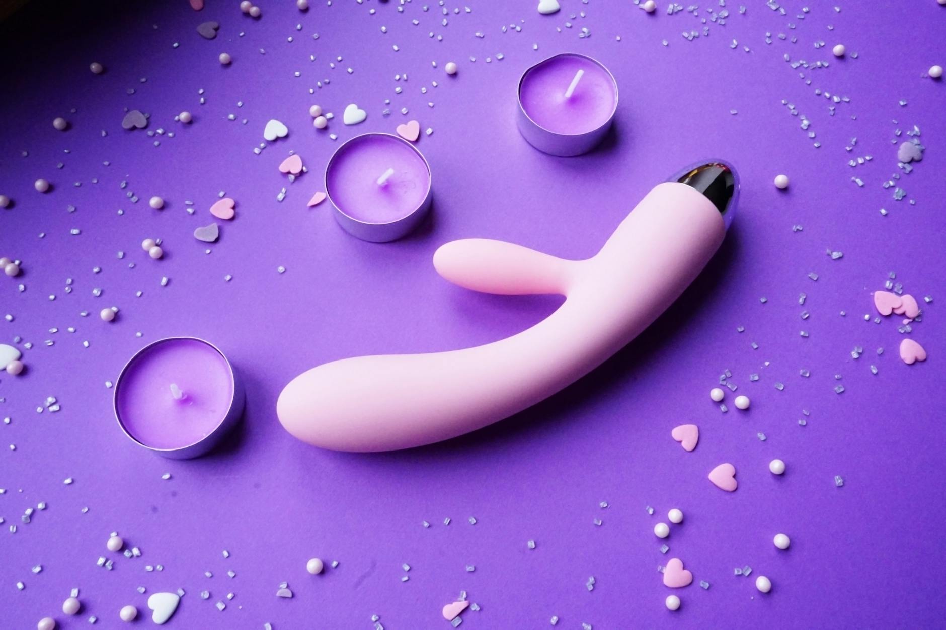 Pink lemon clitoral vibrator on a purple background with heart confetti and candles for a romantic setting